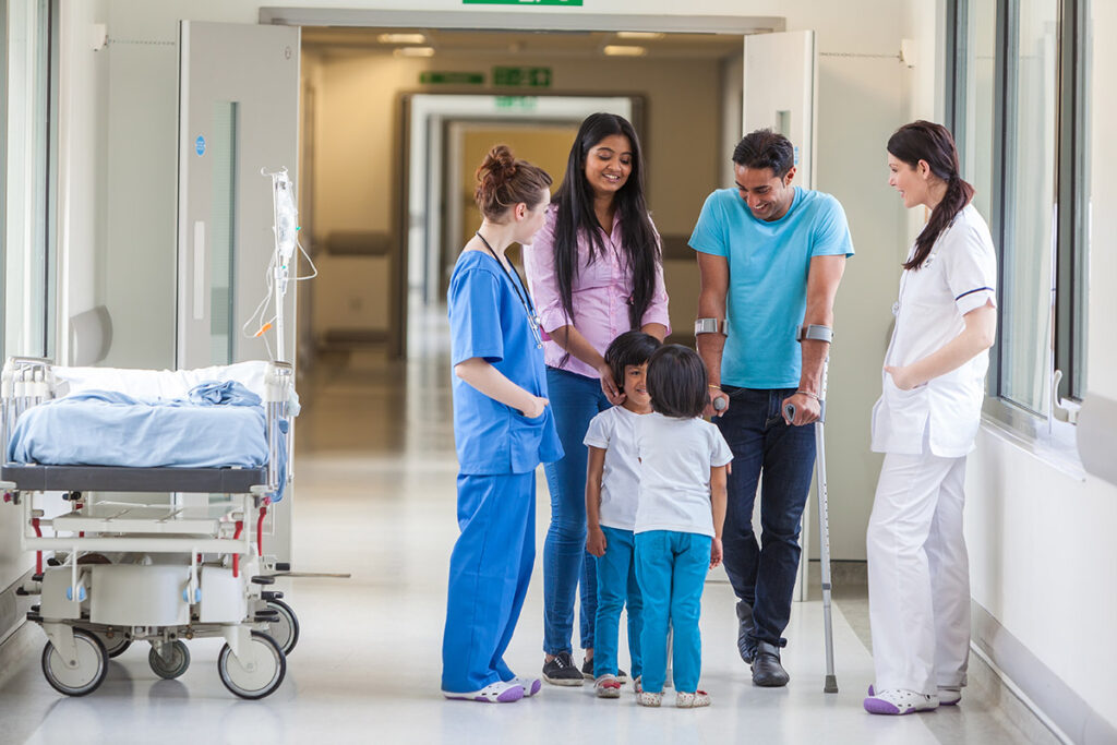A family gathered in the halls of a hospital as they chat with the nurses.