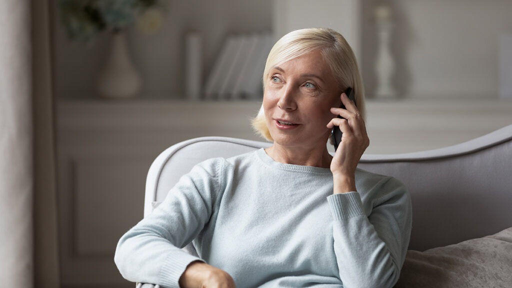 A woman in her 60s on the phone while sitting on the couch.