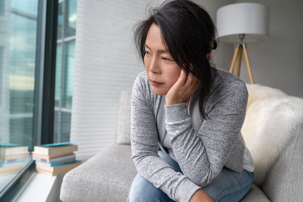 A lone woman in a nice apartment staring out the window at the city beyond, listless.